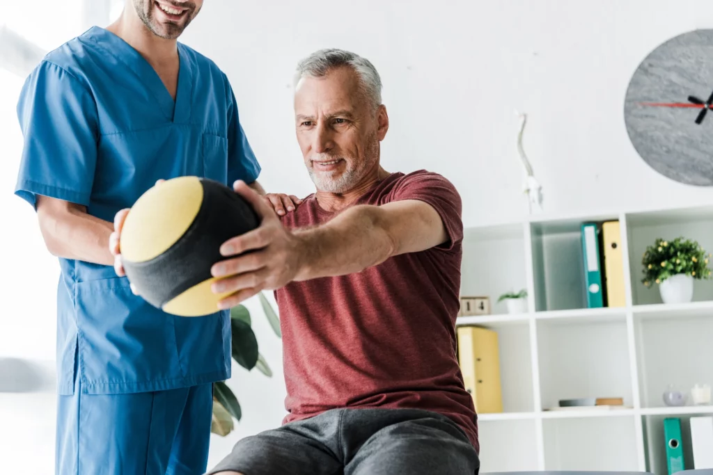 cropped view happy doctor near mature man exercising with ball